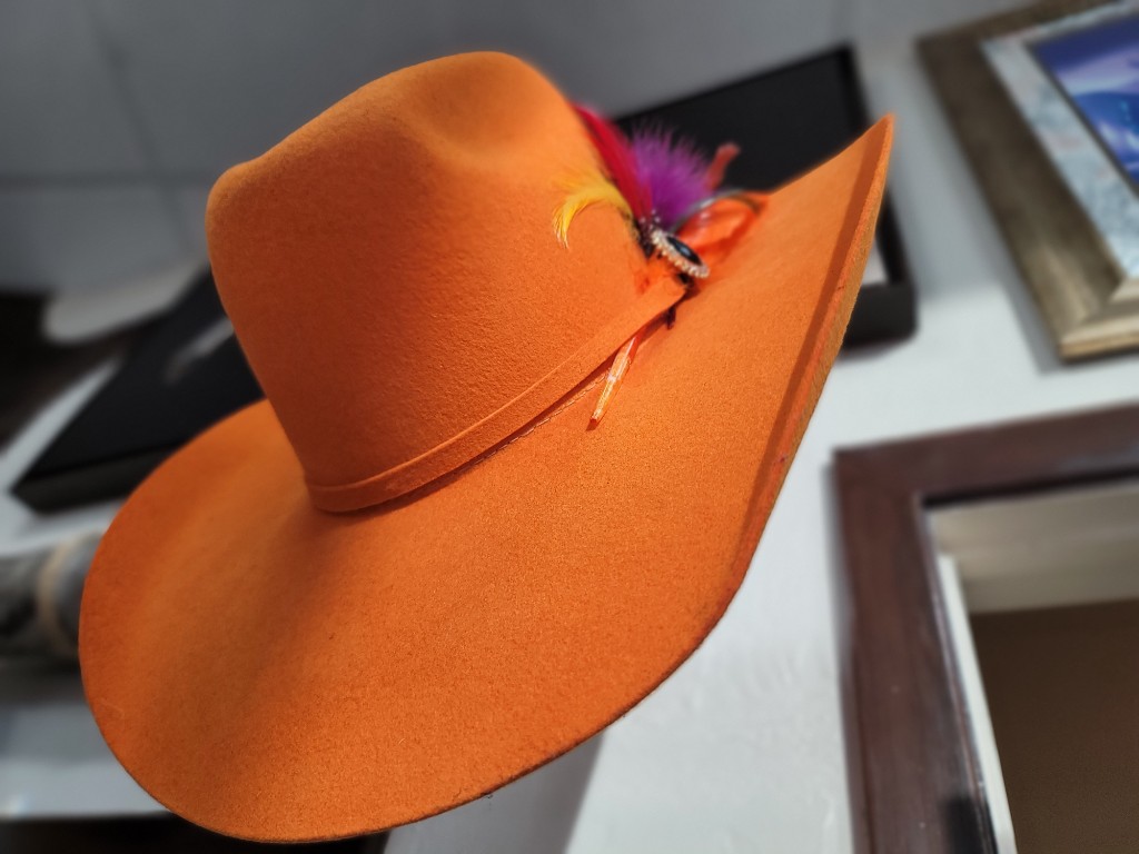 Western GQ luxury fashion — bright orange felt cowboy hat with feather and crystal pin, side view