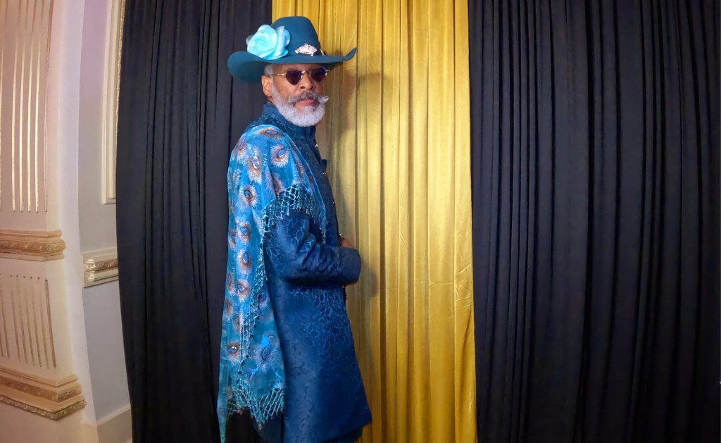 Western GQ luxury fashion — teal cowboy hat, blue coat and peacock-pattern scarf against gold curtains