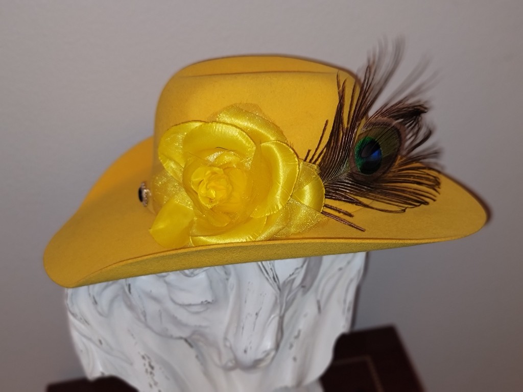 Western GQ luxury fashion — mustard yellow felt hat with fabric rose and peacock feather on white bust
